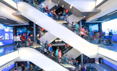 Customers clients moving on escalator staircases inside of giant modern shopping mall. Consumption...