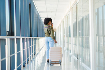 Young african american female passanger in casual clothes is in airport with baggage.