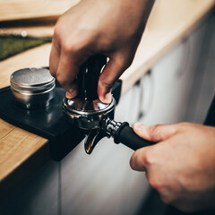 Professional barista temper presses ground coffee in a holder - brewing in a coffee machine