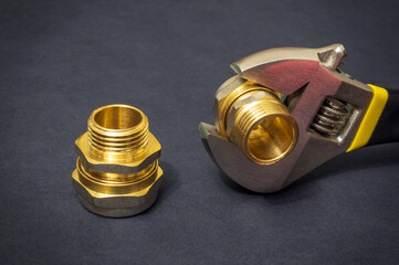 Plumbing brass fittings and adjustable spanner close up on black background during repair or...