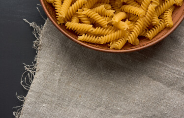 twisted pasta in a round fusilli  on a wooden plate, top view