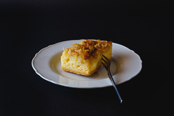 A slice of apple pie on white plate with a dessert fork against black background