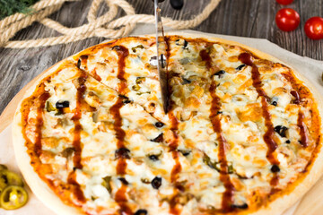 A woman's hand in a transparent glove cuts a pizza with a knife.
A slice is cut off from the striped pizza with a knife