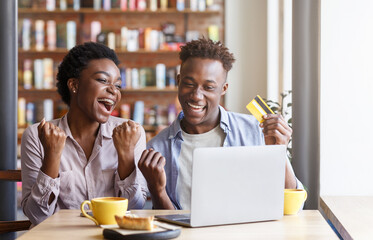 Happy black couple with credit card and laptop shopping online at cafe