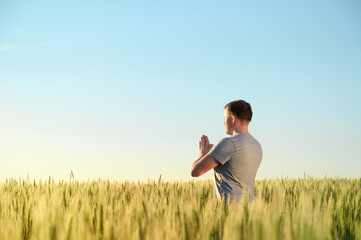Naklejka na ściany i meble Adult man stands on a field in tall grass doing yoga during sunrise. Mental health, connection with nature concept. Copy space.