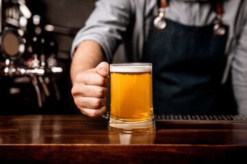 Fototapeta na wymiar Barman in apron serves beer in glass mug on wooden bar counter