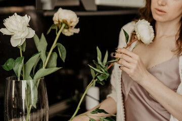 Young attractine woman makes a bouquet of white peonies in a vase