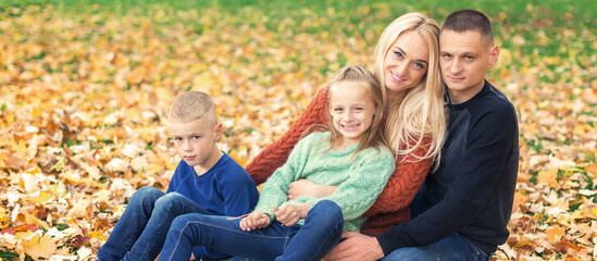 Fototapeta premium Portrait of young family sitting in autumn leaves. Parents with children sitting in the autumn park