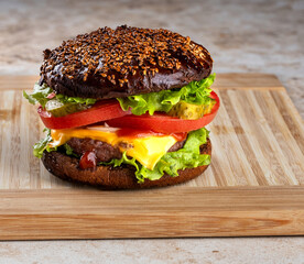 classic american homemade burger on the kitchen board. Bun with sesame seeds, pickled cucumbers, cheddar cheese, tomatoes, onions, meat cutlet.