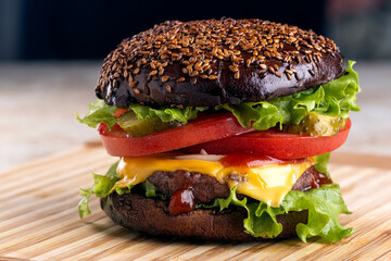 classic american homemade burger on the kitchen board. Bun with sesame seeds, pickled cucumbers, cheddar cheese, tomatoes, onions, meat cutlet.
