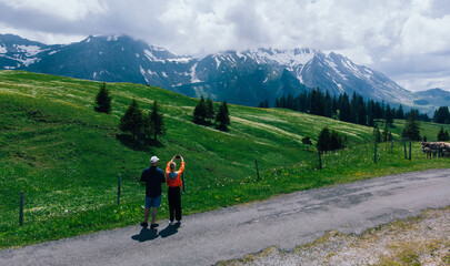 Fototapeta na wymiar Aerial view of couple in love of travellers admiring beauty of picturesque Alpine mountains. Two romantic wanderlusts traveling around world together. Tourist photographing breathtaking view on phone