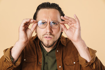 Image of young confused man wearing eyeglasses looking at camera