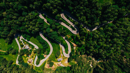 Bird's eye view of scenic serpentine way surrounded by green vegetation. Top view of scenic curvy hairpins in picturesquely mountainous terrain of Italy. Panoramic bike path asphalt road