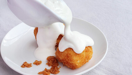 Pouring sour cream on cottage cheese dumplings with a ceramic sauce boat