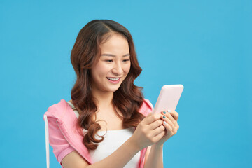 Naklejka premium Portrait of a happy casual girl looking at mobile phone and celebrating isolated over blue background