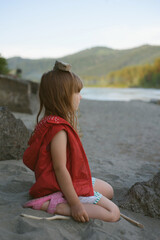 Small girl sits on the sand by the river. Unity with nature, relaxation