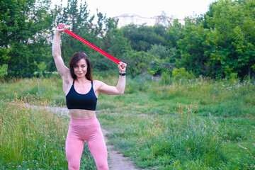 Woman exercising with elastic band outdoors in the park. Young muscle girl.