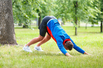 Fototapeta na wymiar Man practice yoga in park. Adult man do downward facing dog pose.
