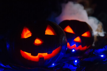 Two glowing pumpkins in the dark in the smoke in the forest close-up. One pumpkin peeks out from behind another. Beautiful background for Halloween.