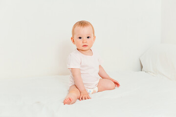 Fototapeta premium Baby in a diaper and T-shirt sits on the bed