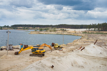 Sand quarry mining industry equipment excavator tractor standing sand land near lake water