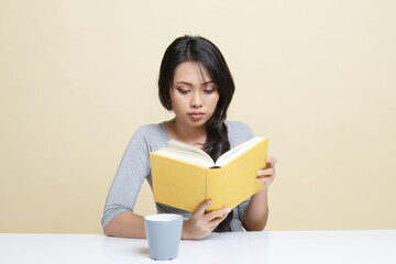 Naklejka premium Young Asian woman read a book with cup of coffee.