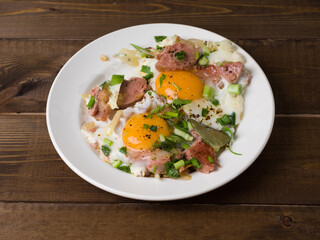Homemade fried eggs with sausage and herbs. White plate on wooden boards