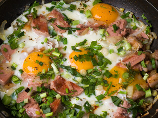 Homemade fried eggs with sausage and herbs. Frying pan on wooden boards. Close-up