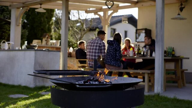 Fire burning on the fire pit in the foreground and family having a picnic in the background on a sunny day