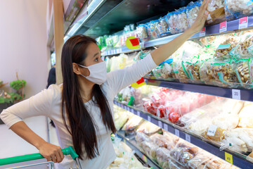 Asian woman wearing wearing protective face mask push and hold shopping cart in supermarket department store. Girl, looking grocery to buy  some food. New normal after covid-19. Family concept.
