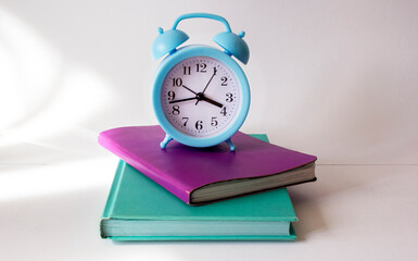 Naklejka premium Colored notebooks and blue alarm clock on a white background