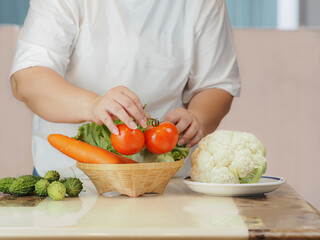 The hands of women aged 50-60 are putting vegetables in a wicker basket on the table , the benefit of fresh vegetables are good for the health of the elderly.