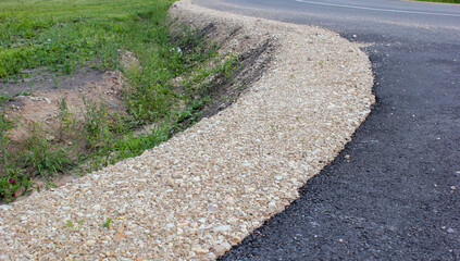 View to a winding new asphalt road in a rural area. Gravel roadside, ditch for rainwater. Latvia. 
