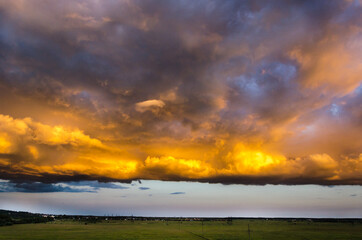 A large Cumulus cloud, illuminated by the setting sun, hovered over a green field.