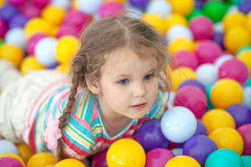 Little cute girl plays in bright colored plastic balls, a child's leisure.
