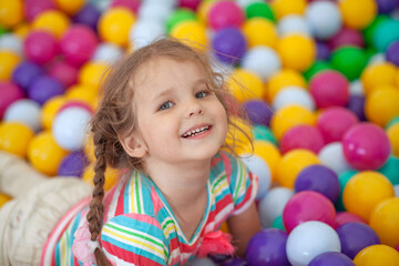 Little cute girl plays in bright colored plastic balls, a child's leisure.
