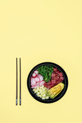 Top view of tuna poke bowl with rice, avocado, wakame, radish and cucumber on yellow background