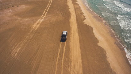 Aerial photo from flying drone of a riding rental car on a sandy beach near beautiful sea with calm...