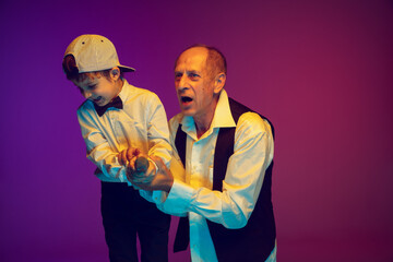 Senior man having fun and spending time together with boy, grandson in neon light. Joyful elderly lifestyle, family, childhood, communication, tech concept. Enjoying singing with microphone. Copyspace