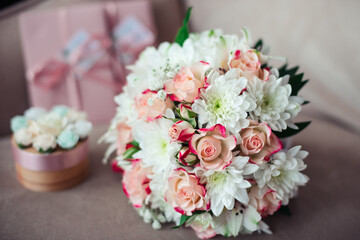 Close-up of a Wedding bouquet of pink roses and white chrysanthemums on a background of pink certificates and a box on a powdery sofa
