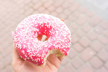 Bitten pink donut in hand. doughnut with a pink chocolate frosting. Sweet dessert festive....