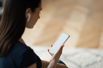 Girl With Earbuds Holding Smartphone Listening To Music Sitting Indoors