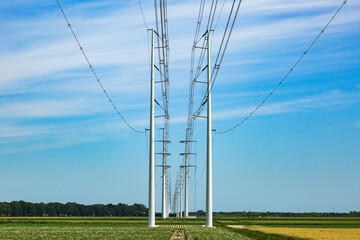 Modern electricity pylons in the countryside under a blue sky with white high clouds
