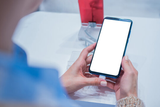 Mockup image: woman customer testing new model of smartphone with blank white display at electronic shop, store, trade show, exhibition. Mock up, copyspace, white screen, template, technology concept