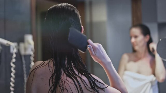 Woman drying and combing long hair in bathroom with hairdryer.