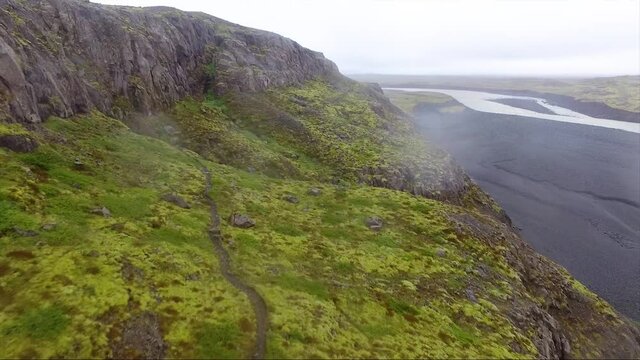 Aerial, drone shot over a hillside trail, on the side of a river delta, in Jokulsarlon national park, on a rainy and foggy day, in Iceland