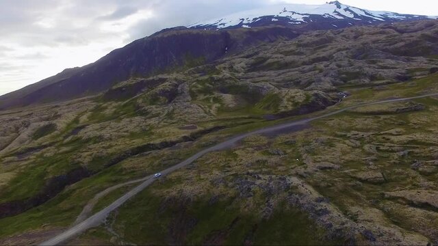 Aerial, drone shot following a white car driving up to the highlands, near Arnarstapi, cloudy day, in Snaefellsjokull national park, in West Iceland