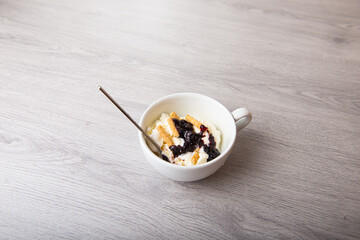 Vanilla ice cream with blackberry jam in a white cup on a wooden light background