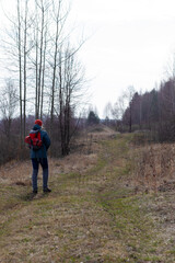 Obraz premium A girl in an autumn jacket, hat and with a backpack takes a walk on nature in early spring. He looks at the vast expanses and enjoys the view.