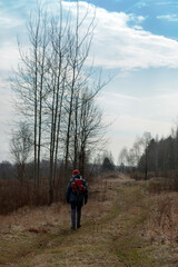 Obraz premium A girl in an autumn jacket, hat and with a backpack takes a walk on nature in early spring. He looks at the vast expanses and enjoys the view.